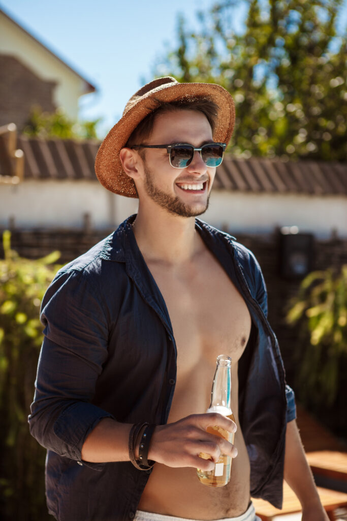 man in sunglasses and hat drinking beer, resting in country house.