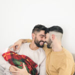 portrait smiling loving gay couple with their baby hand isolated against white backdrop